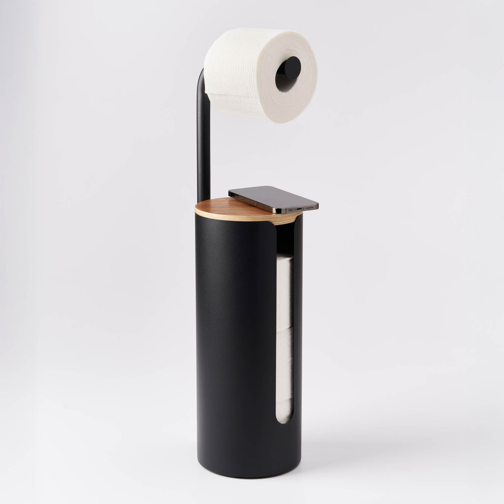 Apto Aloft Toilet Paper Stand with Storage in black with a phone resting on the wood lid and a roll on the arm, shown on a white background