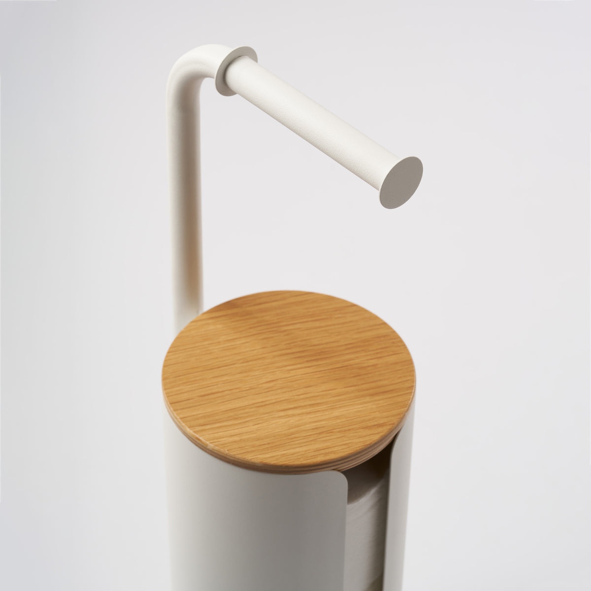 Close-up of the curved white steel arm and round wood lid on the Apto Aloft Toilet Paper Stand with Storage, shown on a white background