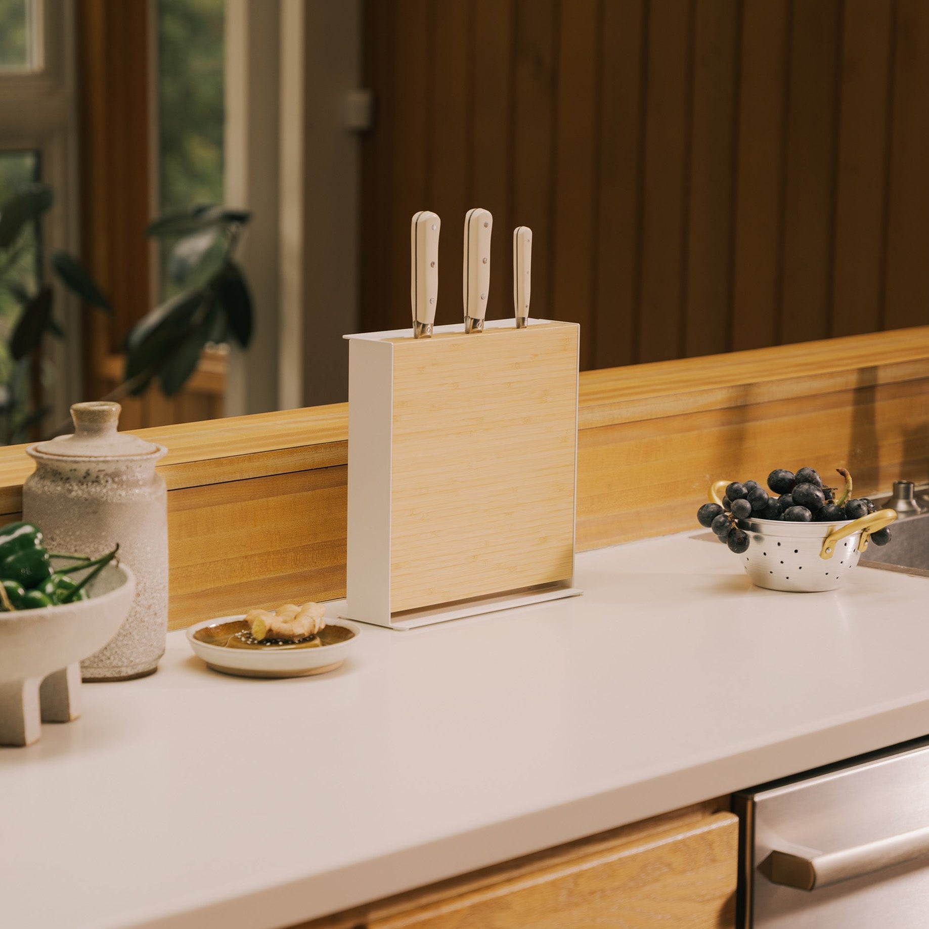 Apto Slot Knife Stand and Cutting Board with the bamboo board slotted in front and three knives on top, set on a white kitchen counter