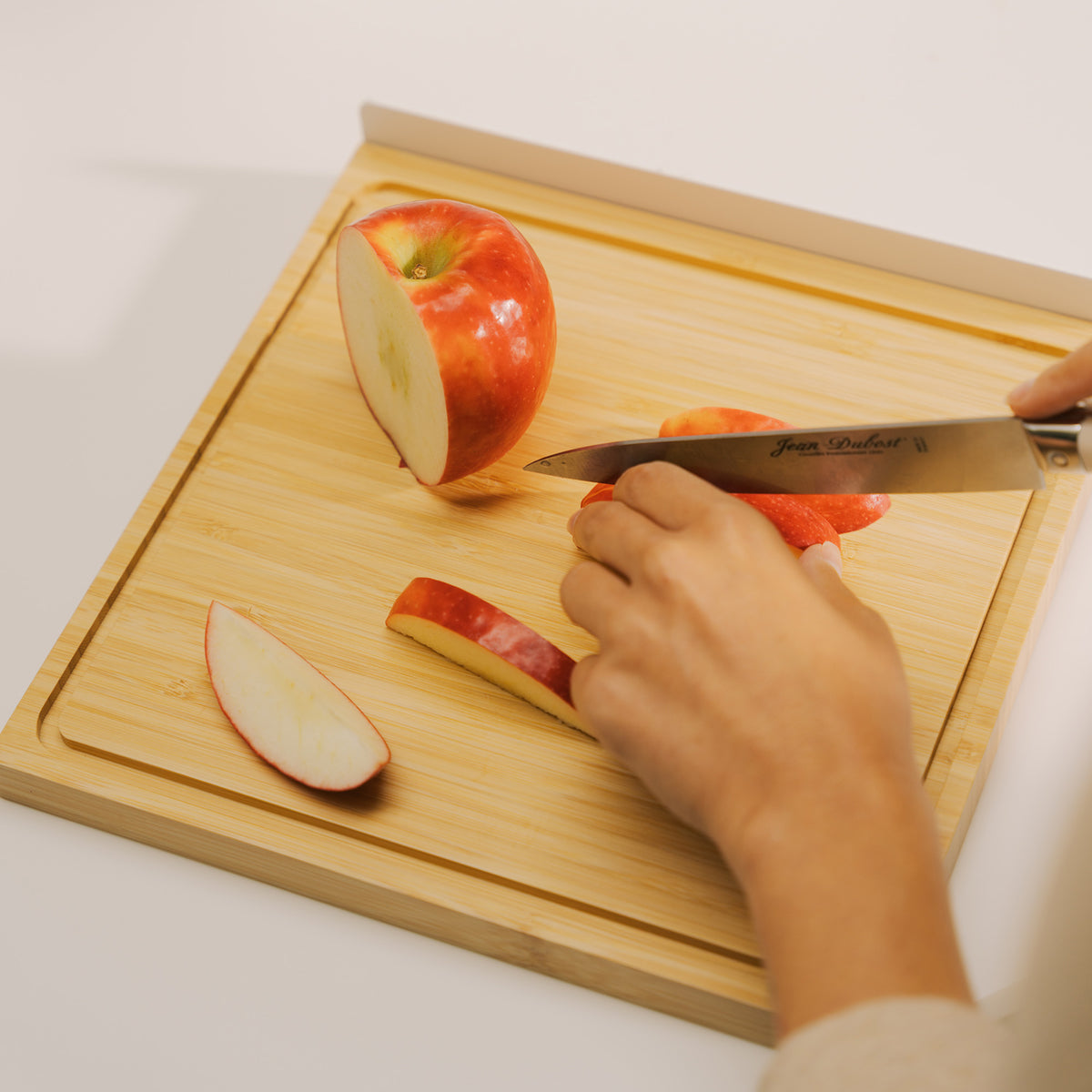 Close-up of hands slicing a red apple with a chef's knife on the bamboo board from the Apto Slot Knife Stand and Cutting Board set
