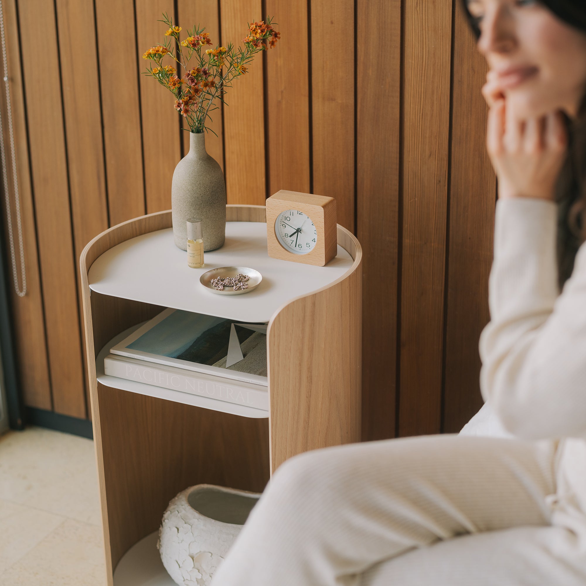 Minimalist ash and white bedside table with rounded corners and storage shelves beside bed in modern bedroom