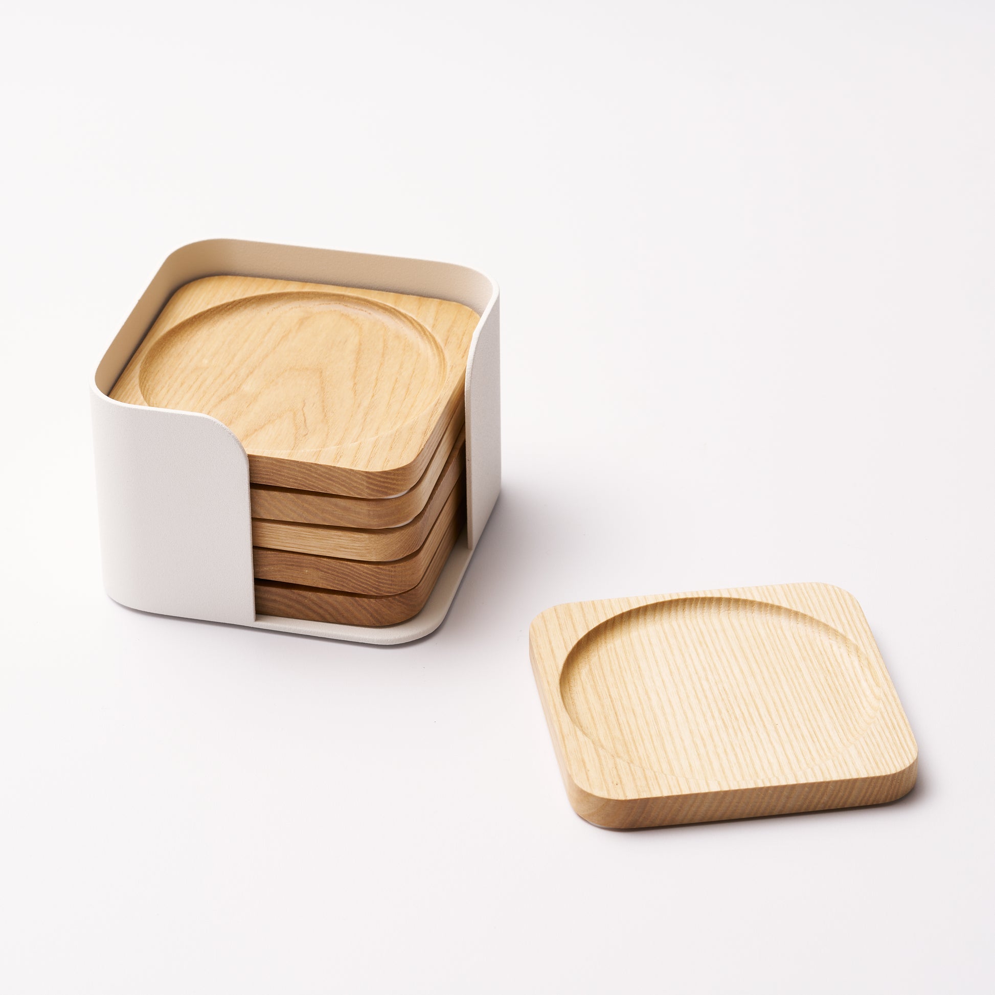 Five natural wood coasters held by a white steel organizer and one coaster displayed on its own on a white background. Designed by Apto. 