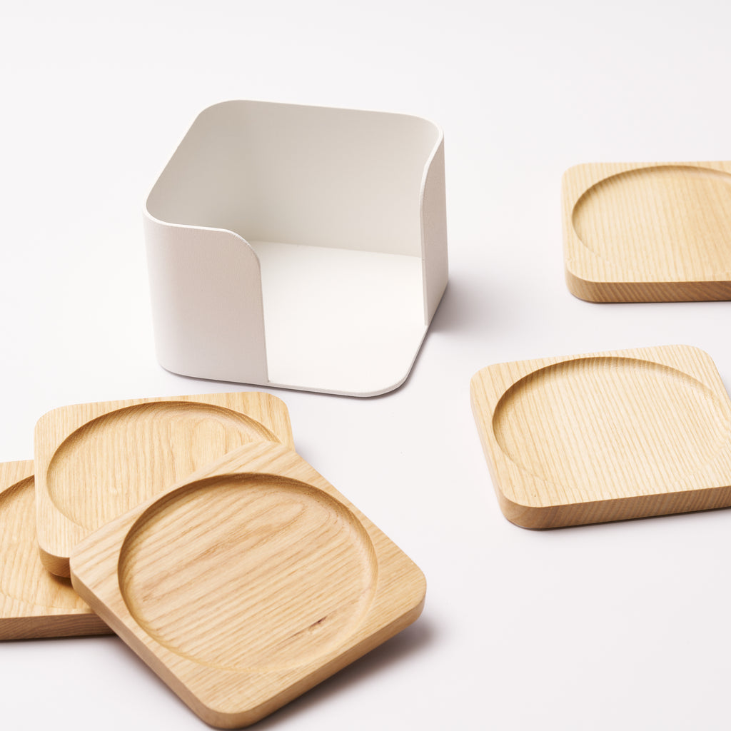 Empty steel coaster holder surrounded by a spread of wood coasters with divets in the center to hold cups, from Apto