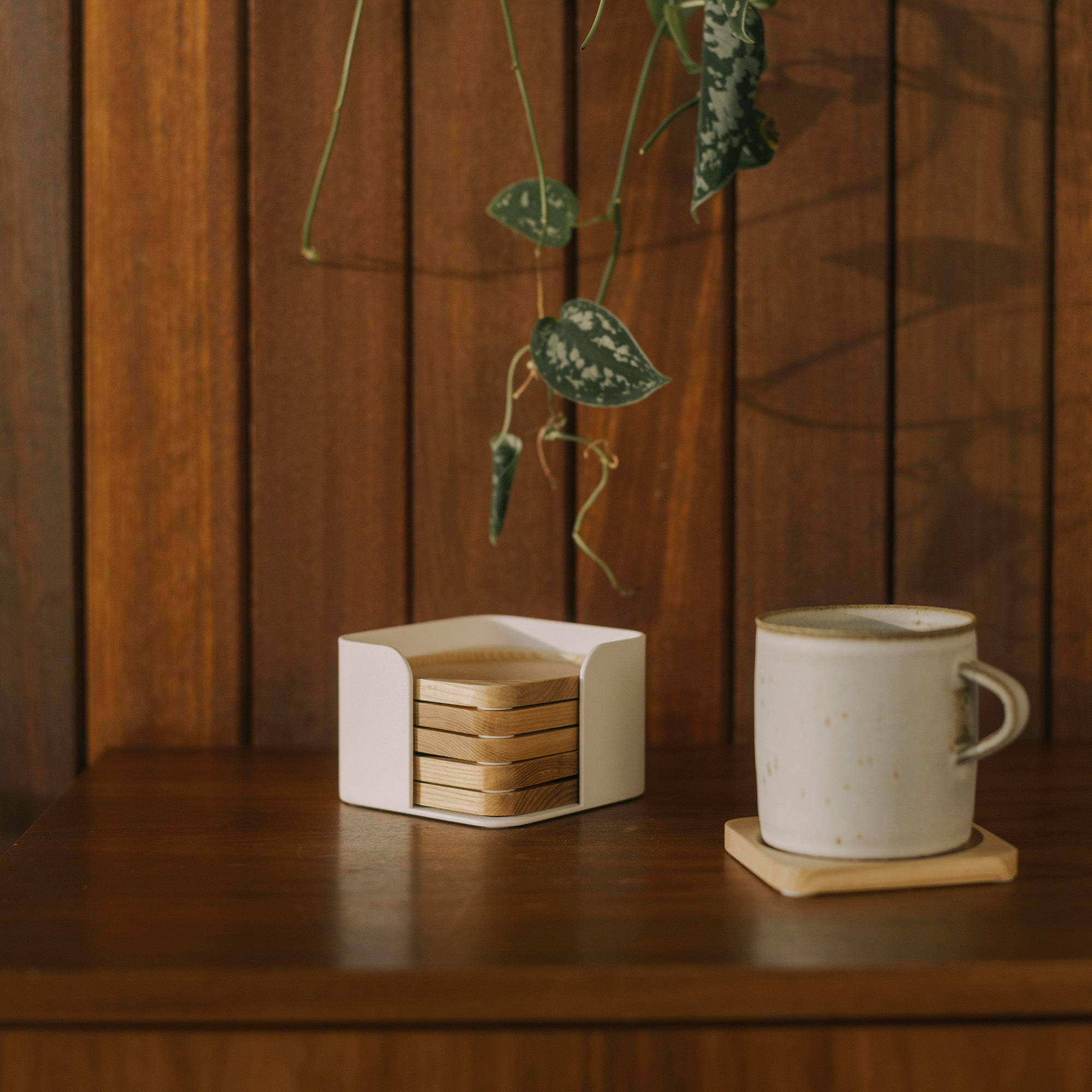 Contour Coaster Set shown with five out of six natural wood coasters in a white steel container and one coaster placed under a ceramic coffee mug in a dark wood living room.