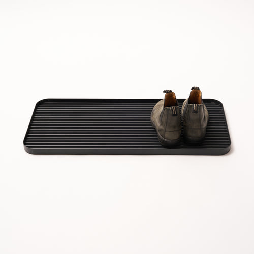 Black steel boot tray with ridged bottom holding a pair of boots with a white backdrop. Designed by Apto. 