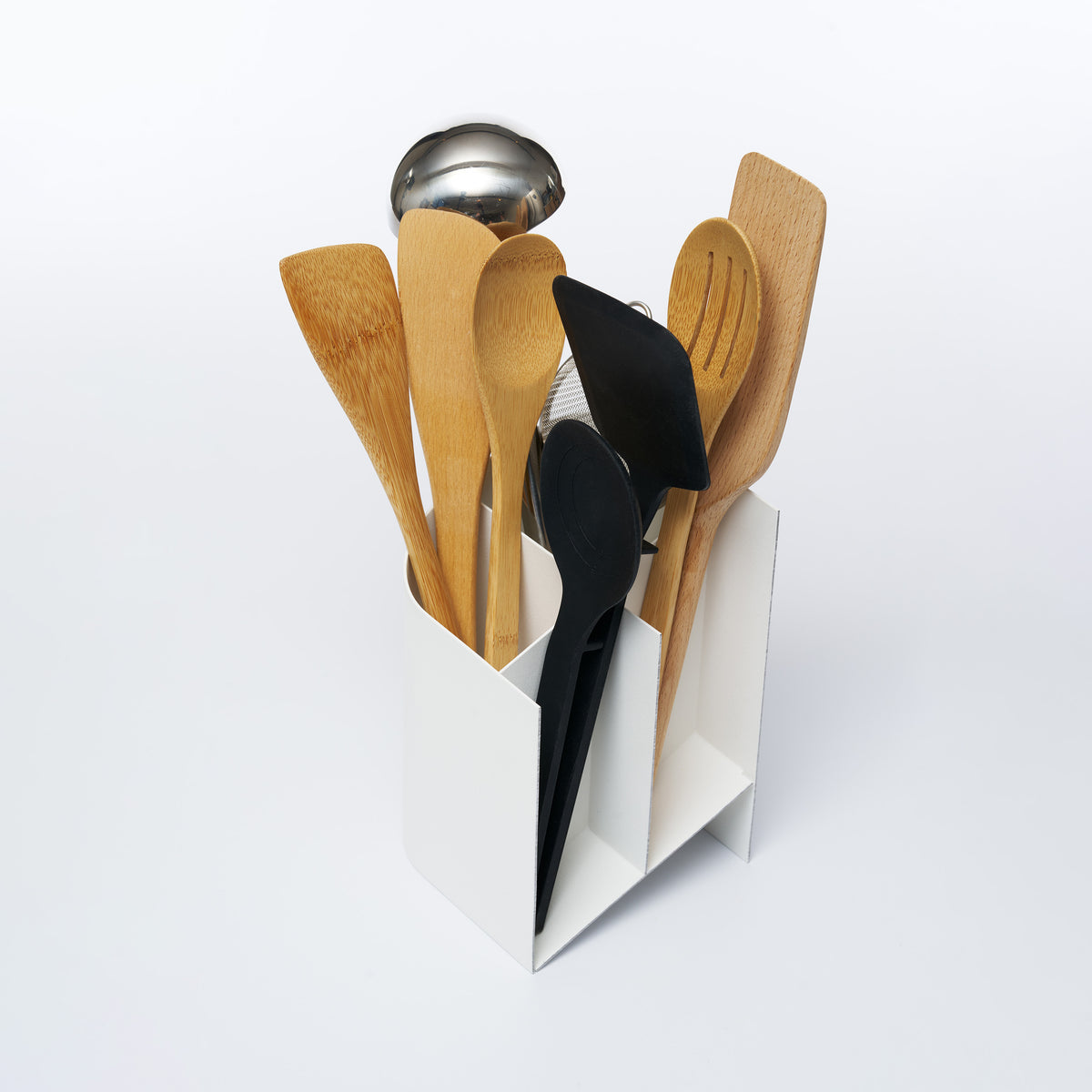 Angled overhead view of Sloped Utensil Holder, shown in a cutaway view revealing its compartments with assorted cooking utensils.