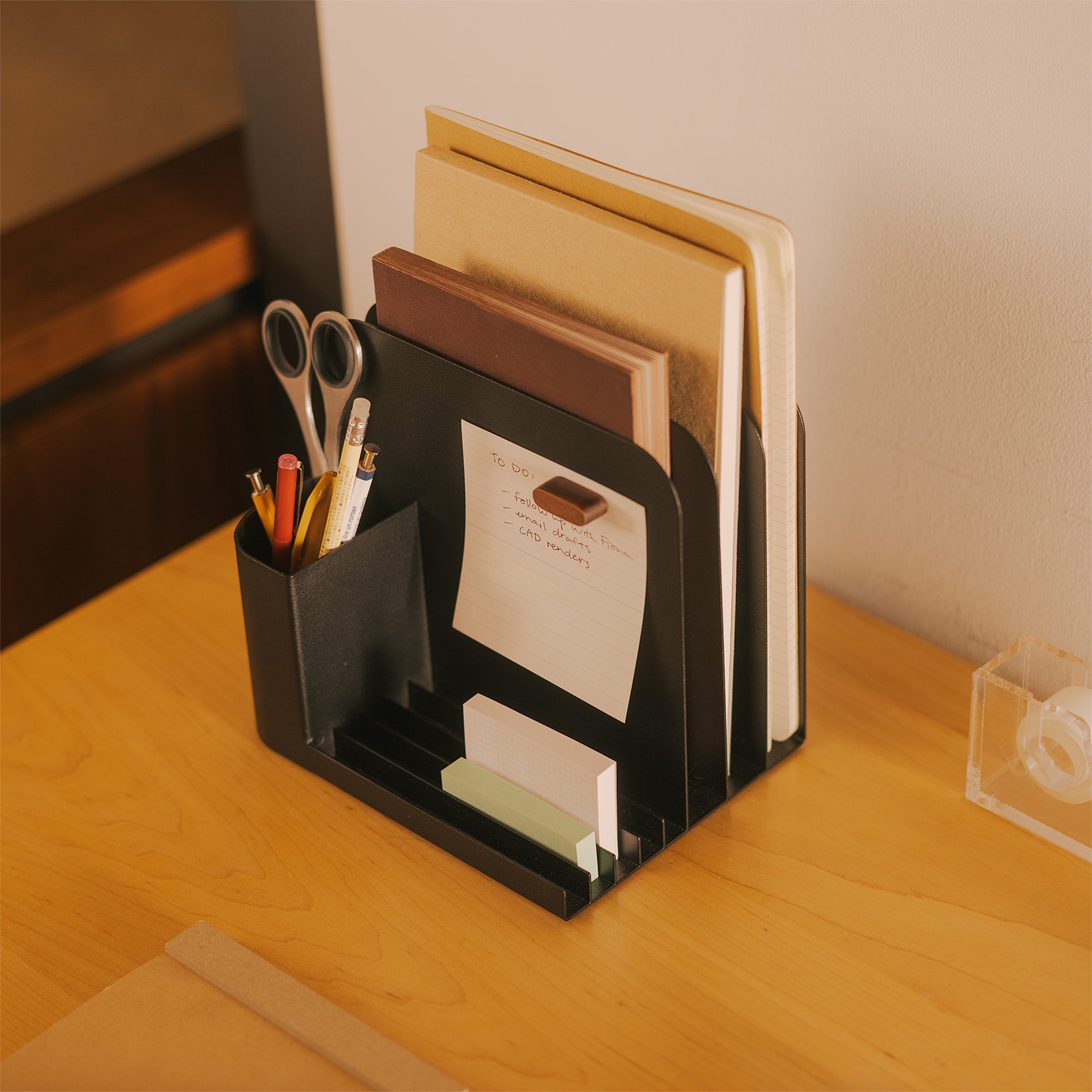 Black steel desk caddy from Apto organizing files, pens, office supplies, and post-its.
