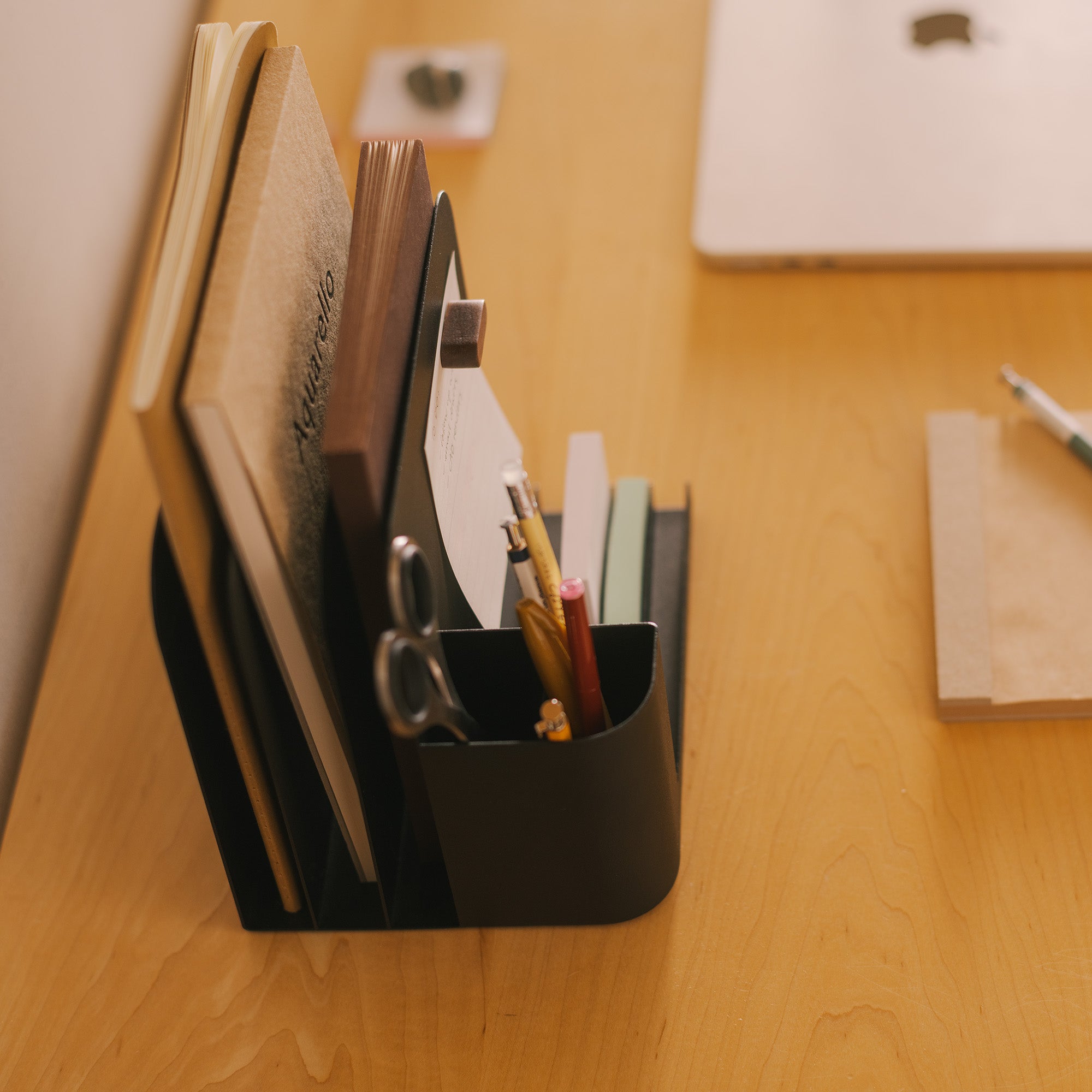 Black steel desk caddy from Apto organizing files, pens, office supplies, and post-its.