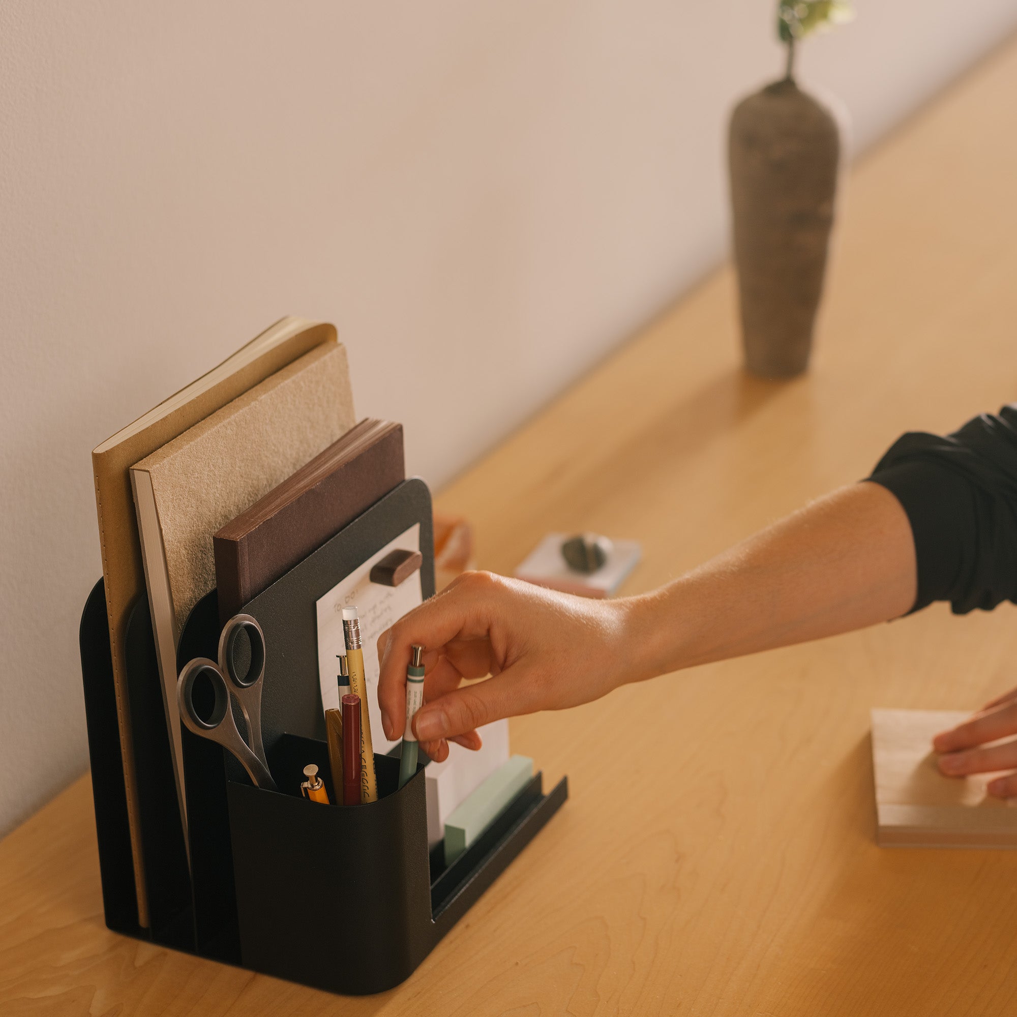 Woman organizes writing supplies in a black steel desk caddy from Apto organizing files, pens, office supplies, and post-its.