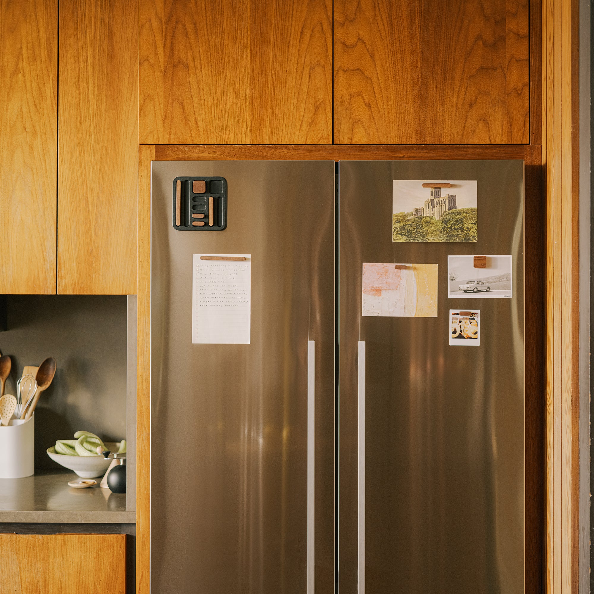 Modern kitchen with warm wood cabinets, stainless steel side-by-side refrigerator, and white utensil holder on granite countertop