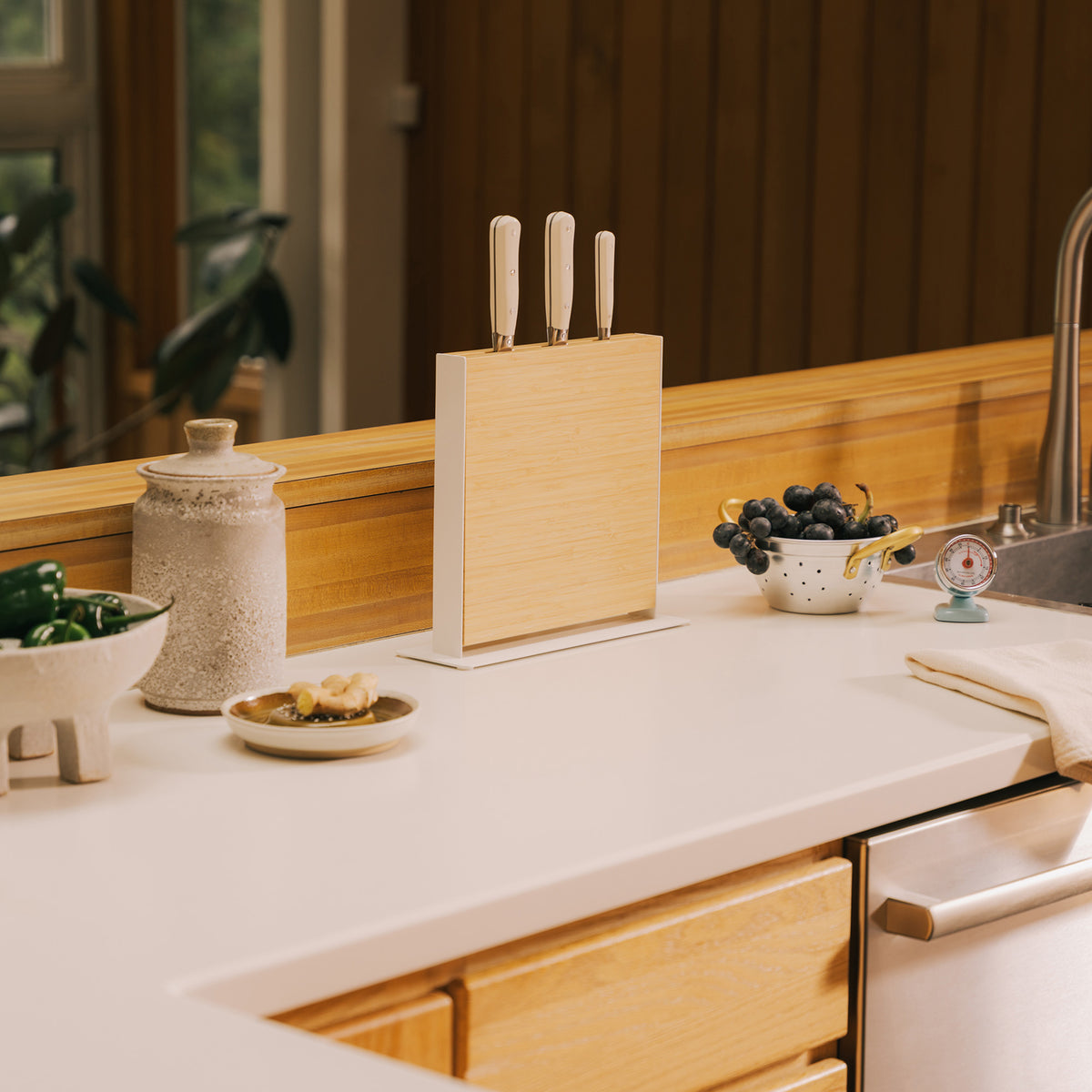 Front view of the Apto Slot Knife Stand in bamboo and white steel holding three knives on a white counter in a warm wood kitchen