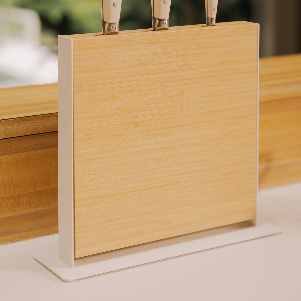 Close-up side view of the Apto Slot Knife Stand showing the bamboo panel set in its white steel frame and base, with knives on top