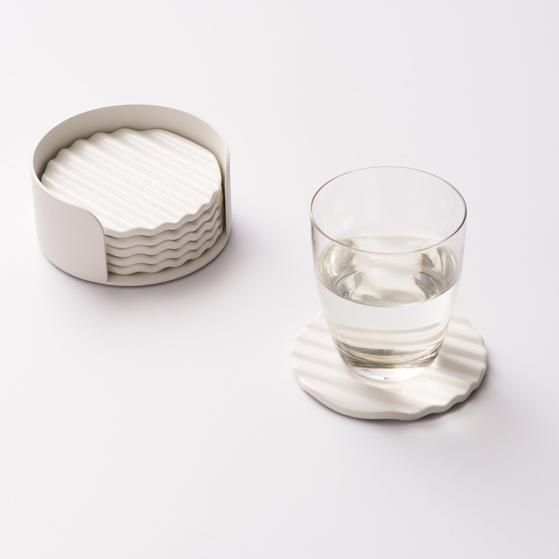 Wave ceramic coaster set in holder with one coaster displayed and holding a glass of water