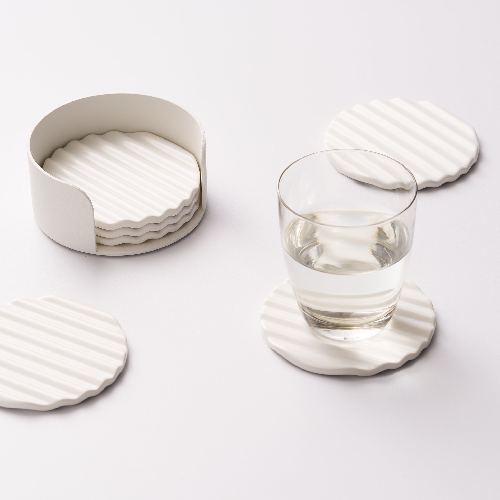 Wave ceramic coaster set in holder with three coasters displayed, one holding a glass of water