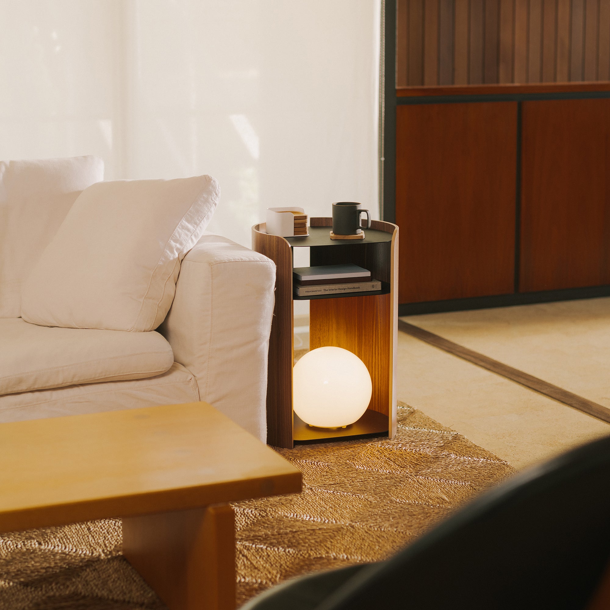 Walnut and black steel modern sidetable holding a globe lamp next to a white couch in a modern living room.