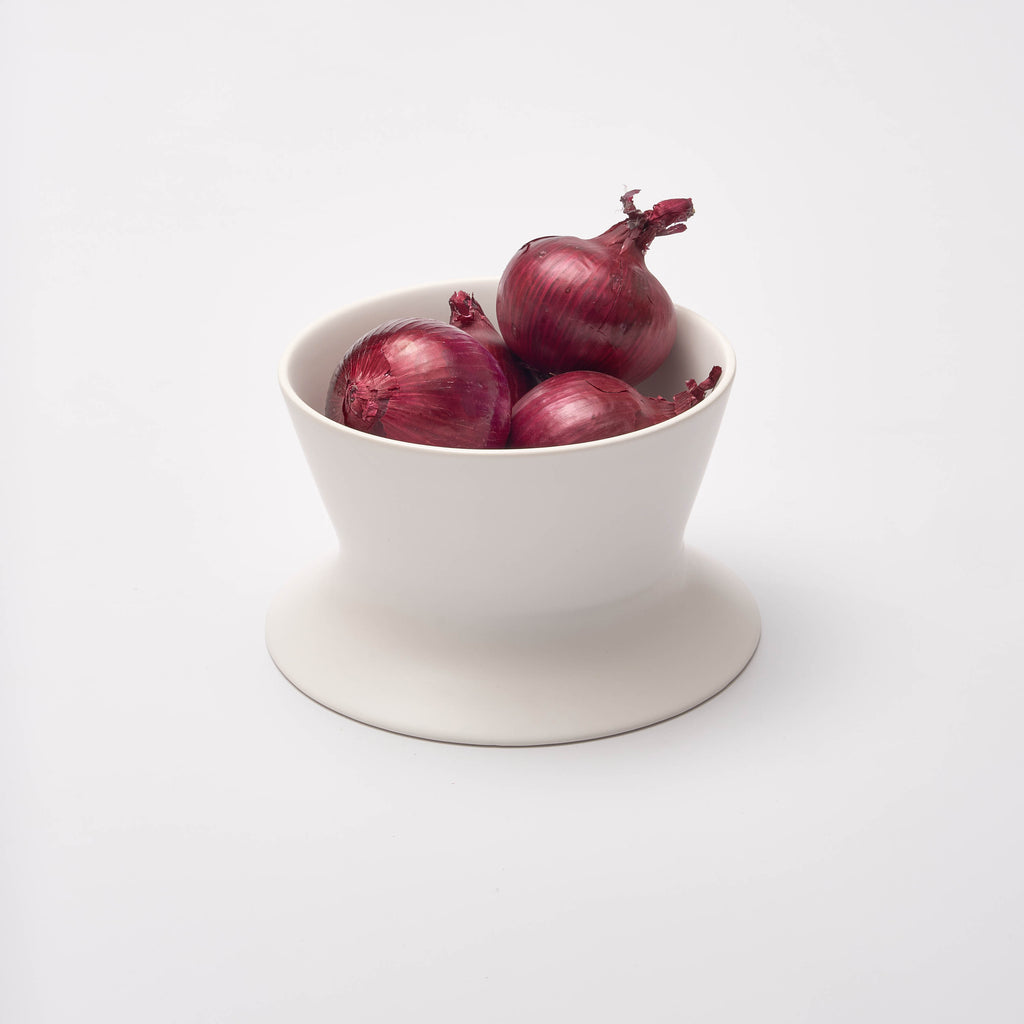 White Apto Flip Fruit Bowl flipped to the deep side, holding red onions, showing how one bowl works two ways, on a white background