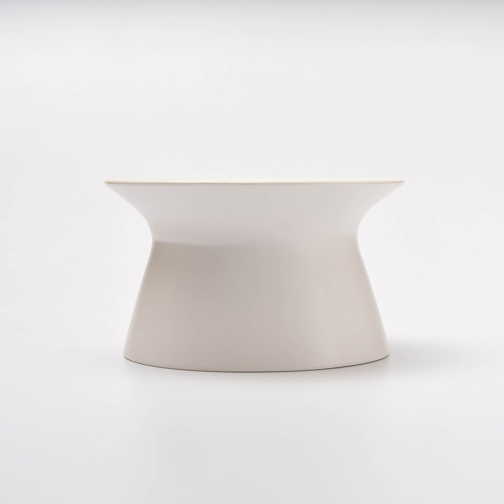 Side profile of the empty white Apto Flip Fruit Bowl, showing its curved hourglass shape that flips for two uses, on a white background