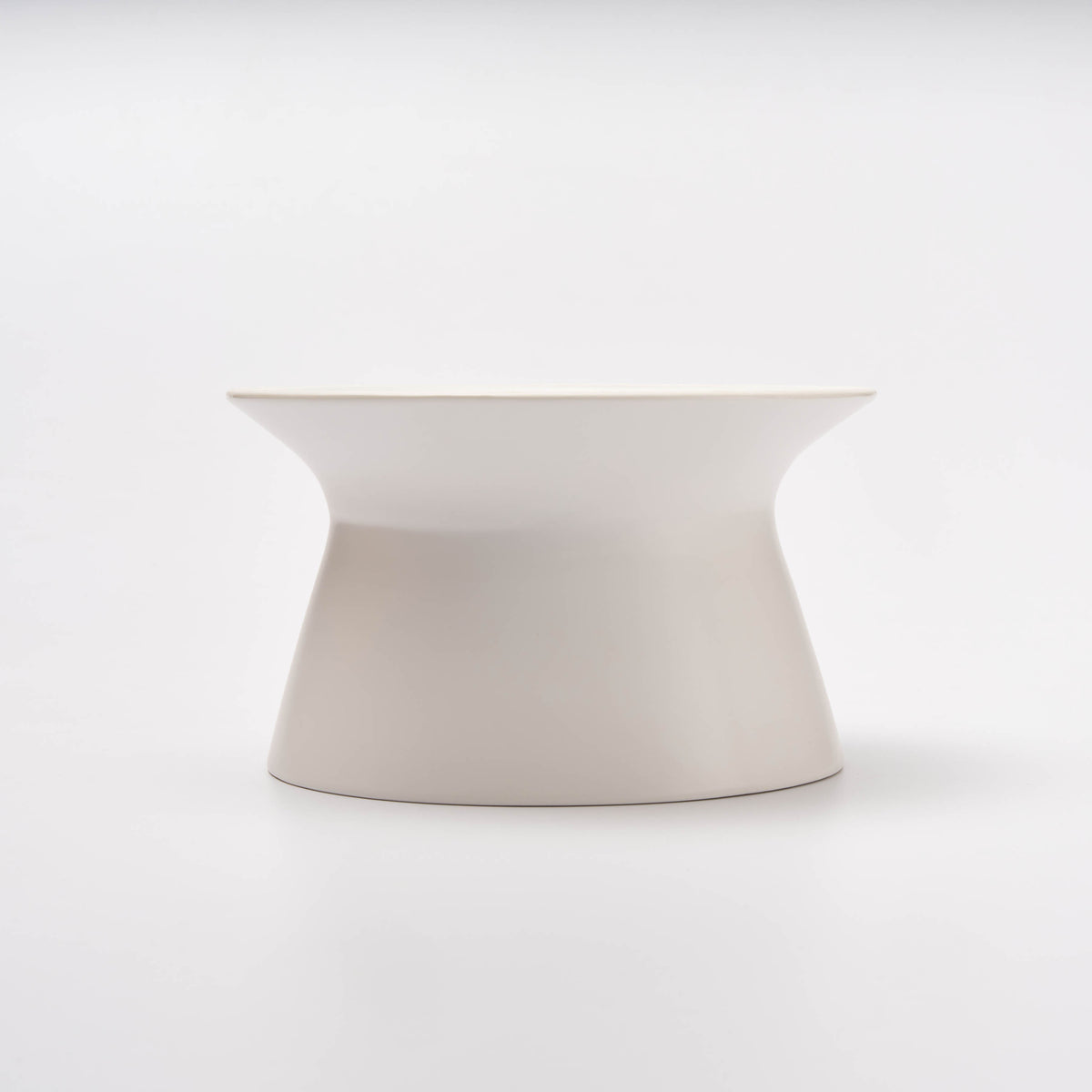 Side profile of the empty white Apto Flip Fruit Bowl, showing its curved hourglass shape that flips for two uses, on a white background