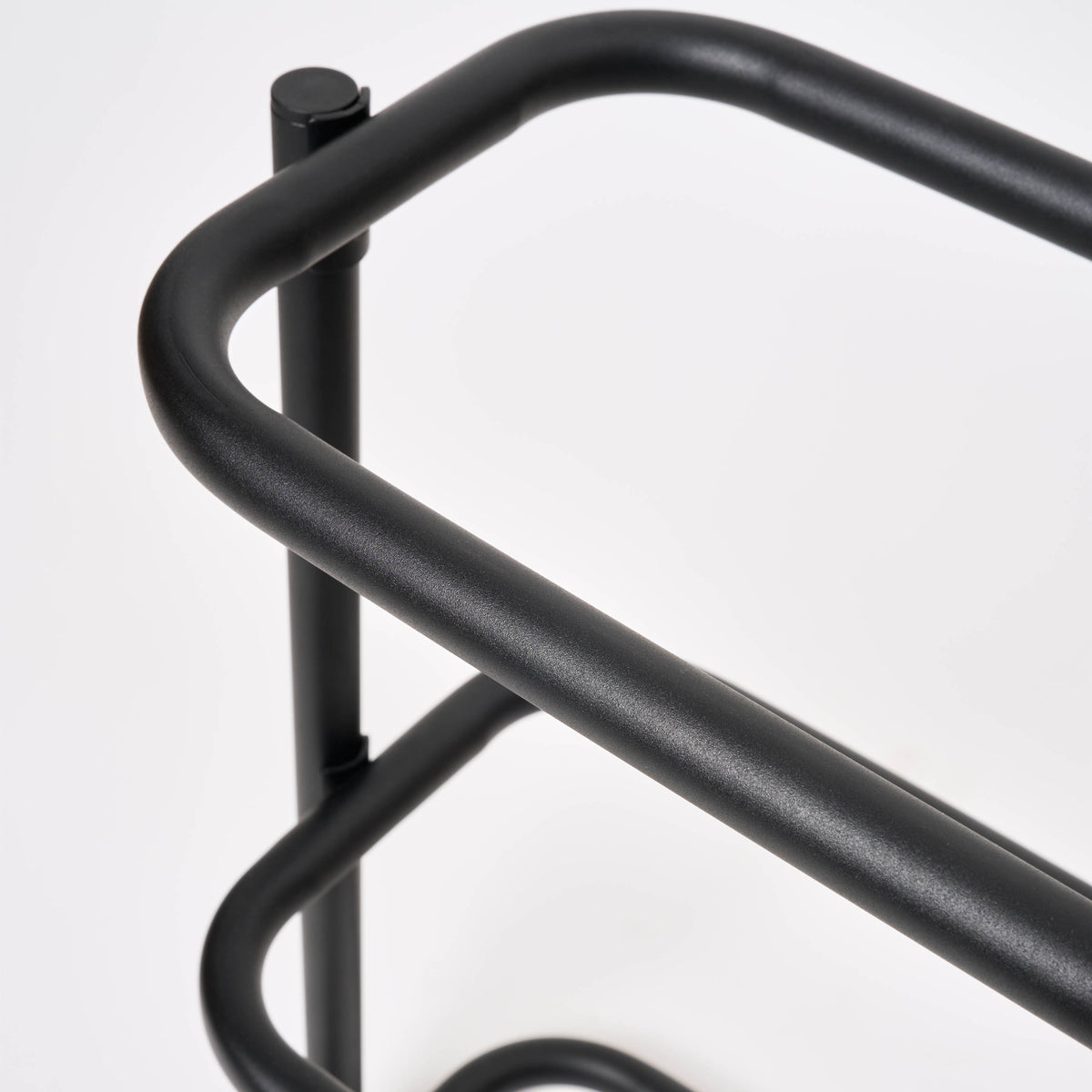 Close-up of the rounded corner on the Apto Obround Shoe Rack Short in black steel, showing the smooth bent tube frame on a white background