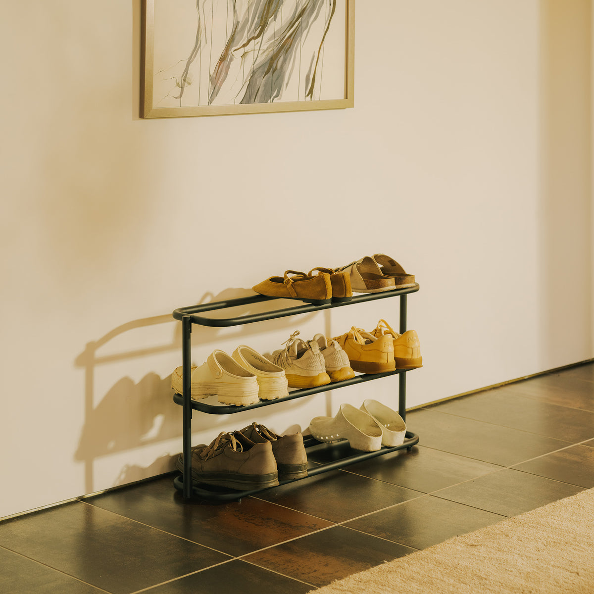 Apto Obround Shoe Rack Short in black steel holding shoes on three tiers in an entryway with a tile floor and framed art above