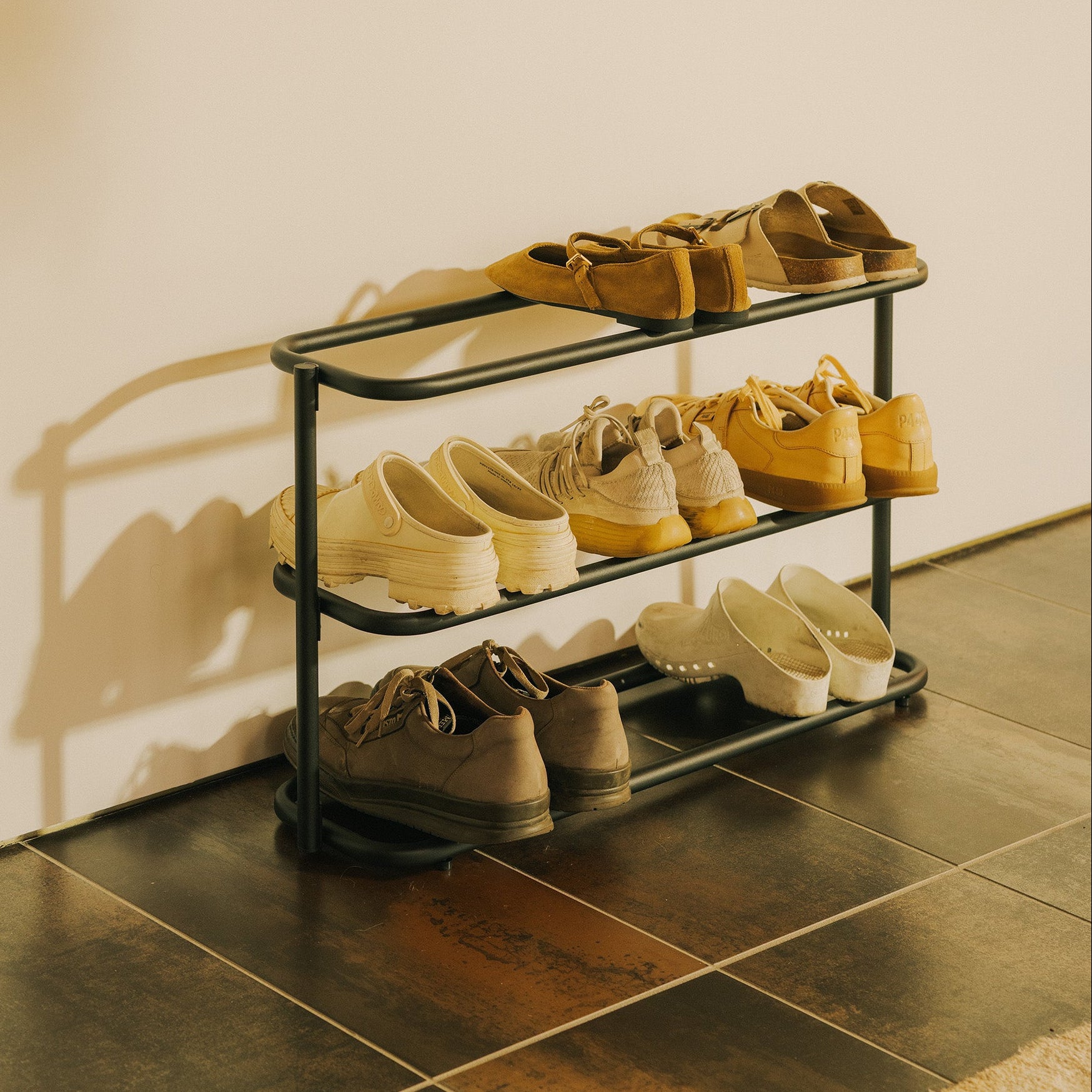 Angled view of the Apto Obround Shoe Rack Short in black steel with sneakers, loafers and sandals on three tiers on a tile floor