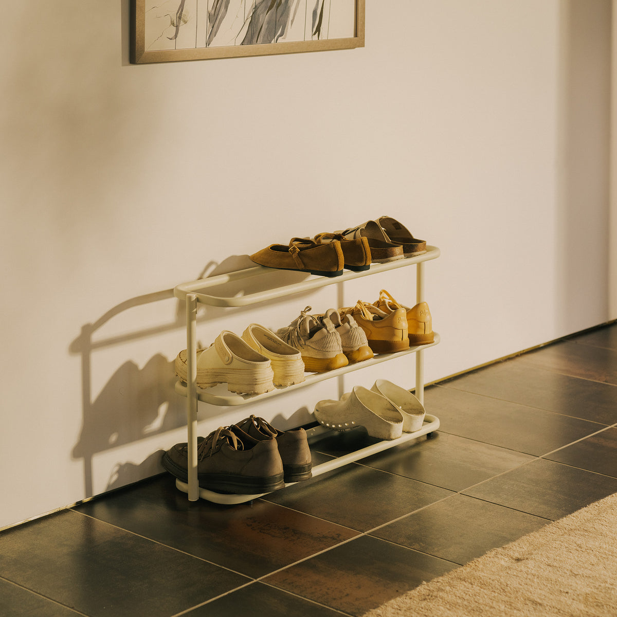 Apto Obround Shoe Rack Short in ivory steel holding sneakers and loafers on three tiers, casting soft shadows in a sunny entryway