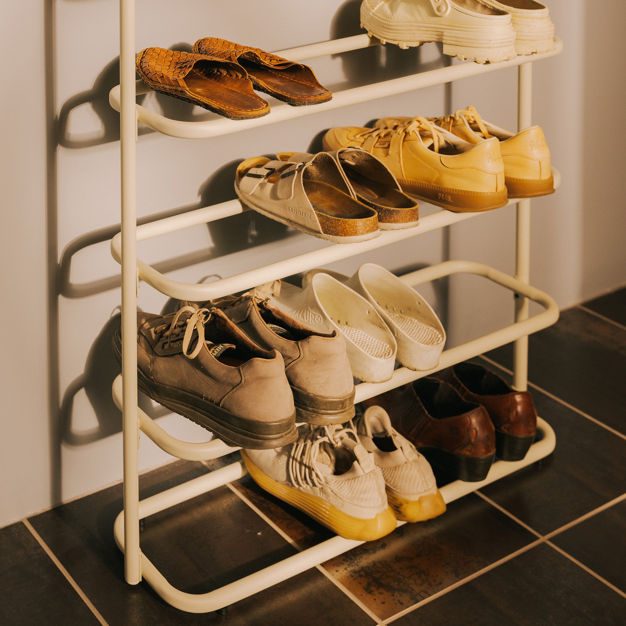 Ivory metal entryway shoe rack on a tiled floor, neatly organized with shoes