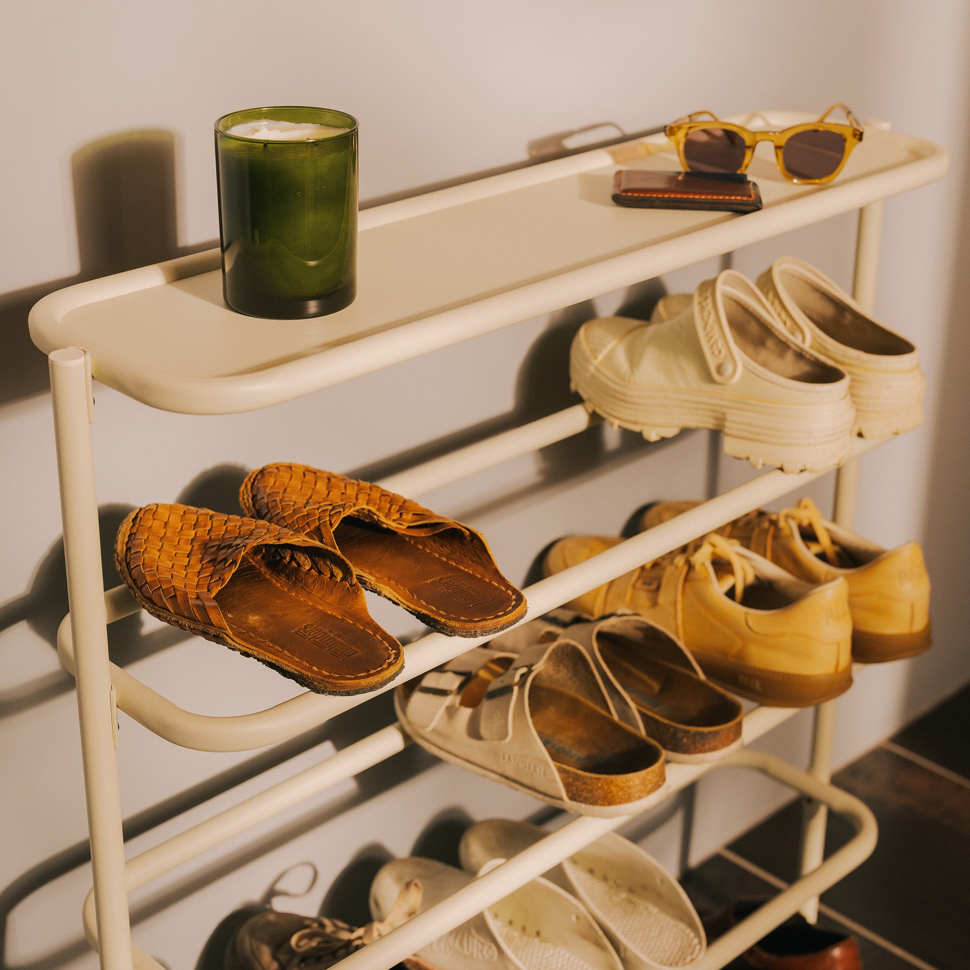 Ivory metal entryway shoe rack with flat top shelf holding sunglasses, candle, card case, organized with shoes