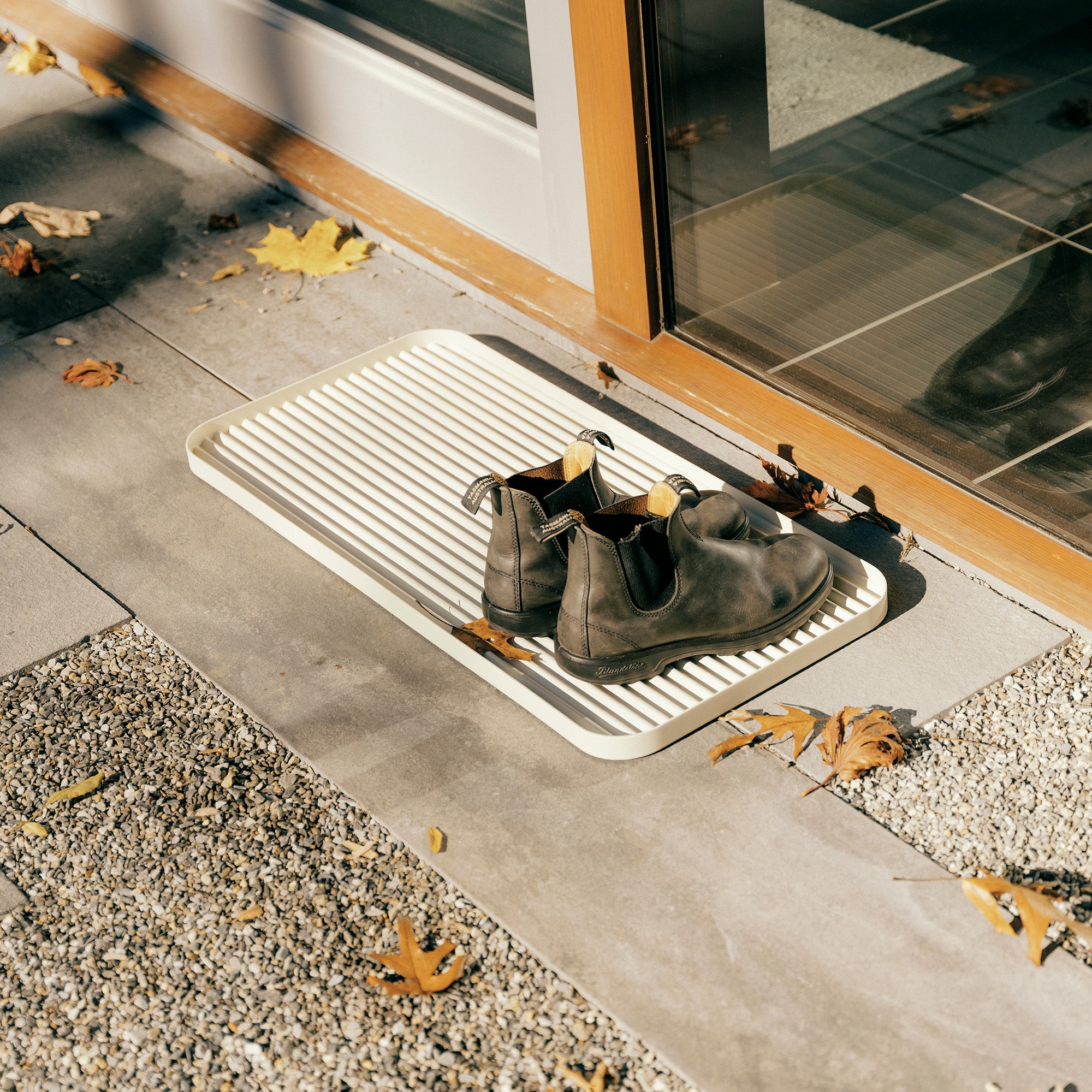 White steel boot tray with ridged bottom holding a pair of Blundstones and gardening supplies outside a modern home.