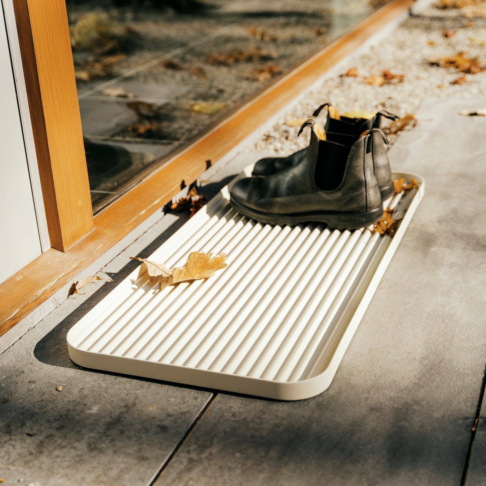 White steel boot tray with ridged bottom holding a pair of Blundstones and fall leaves outside a modern home.