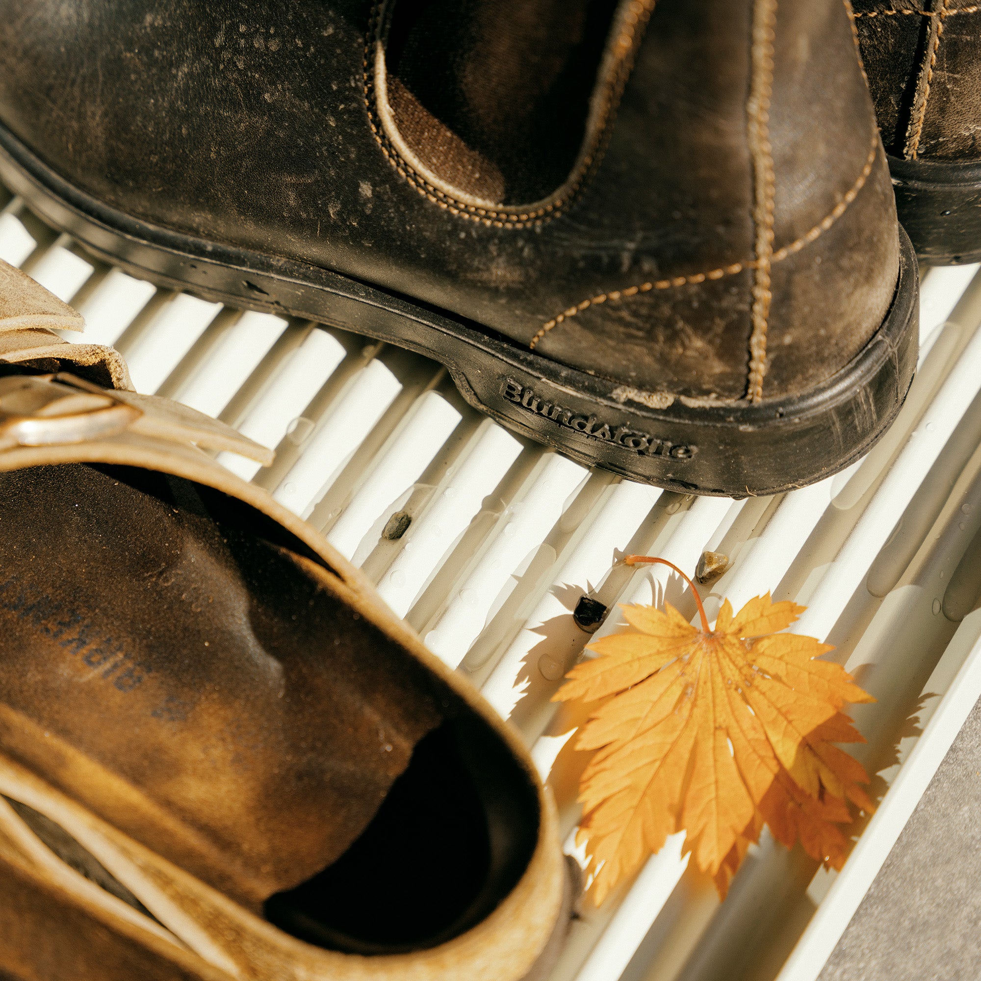 White steel boot tray with ridged bottom holding a pair of Birkenstocks and Blundstones and fall leaves outside a modern home.