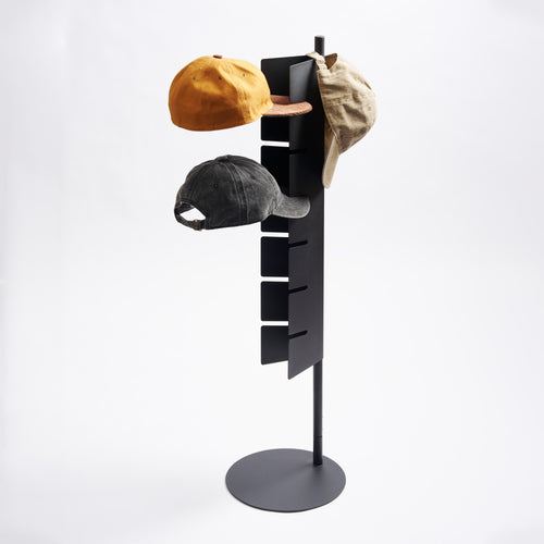 Apto Slot Cap Stand in black steel holding three baseball caps on its slotted panel, with a round base, on a plain white background