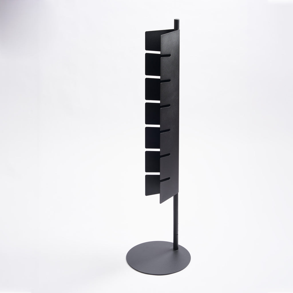 Empty Apto Slot Cap Stand in black steel, showing the tall slotted panel and round weighted base, on a plain white background