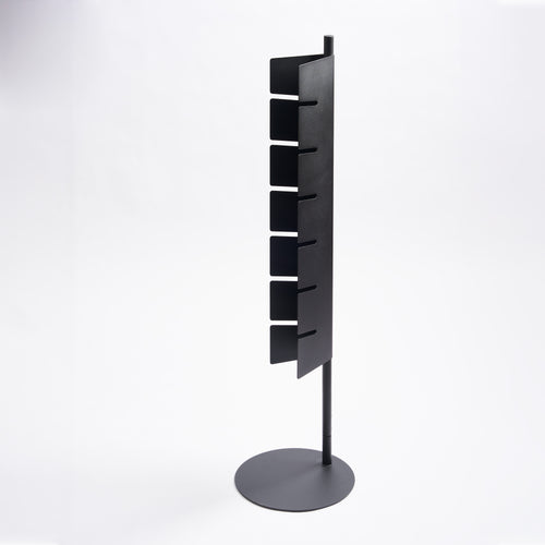 Empty Apto Slot Cap Stand in black steel, showing the tall slotted panel and round weighted base, on a plain white background