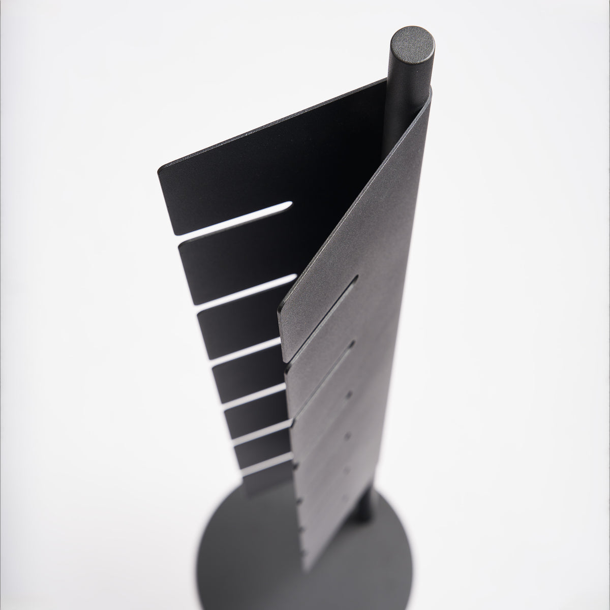 Close-up of the slotted steel panel on the Apto Slot Cap Stand in black, showing the angled slots that hold each cap brim in place