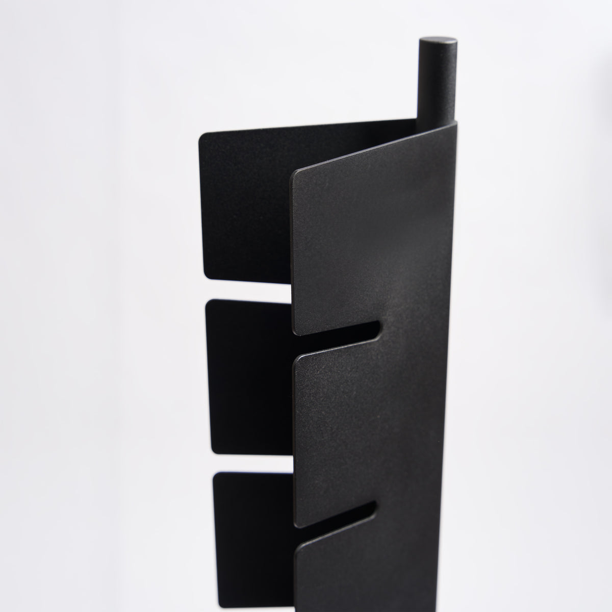 Close-up of the slots on the Apto Slot Cap Stand in black steel, showing how each cap brim slides into place and stays put, on a white background