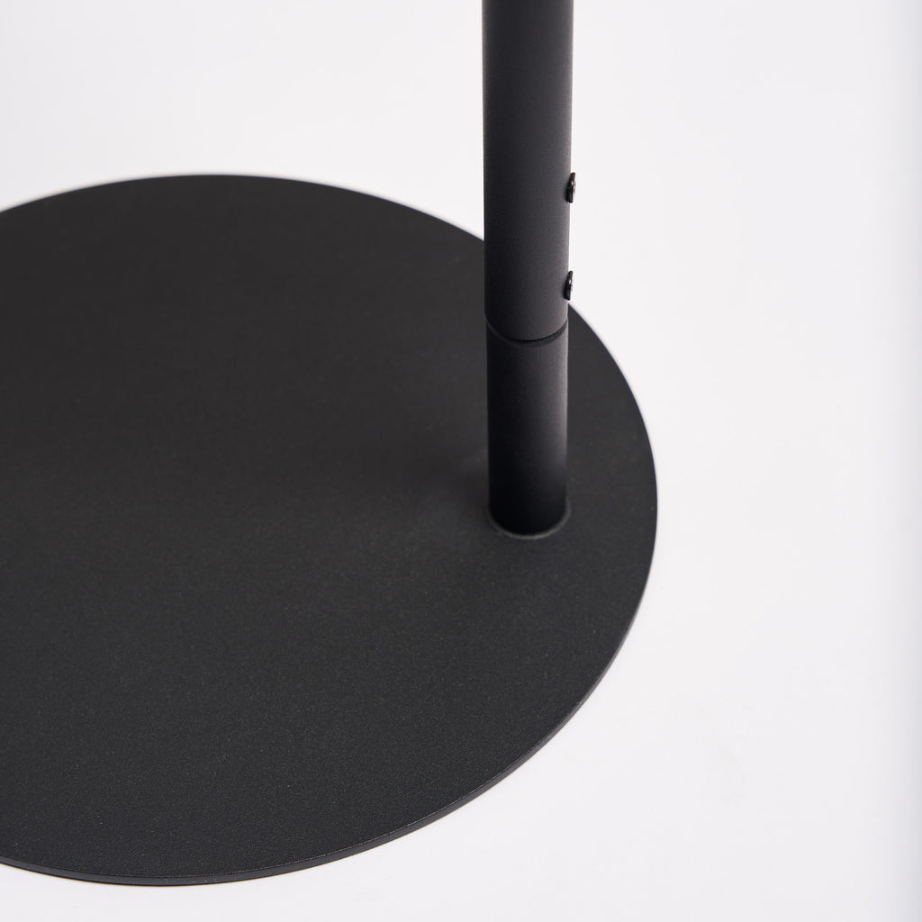 Close-up of the round base on the Apto Slot Cap Stand in black steel, showing the slim pole and the flat, sturdy footprint, on a white background