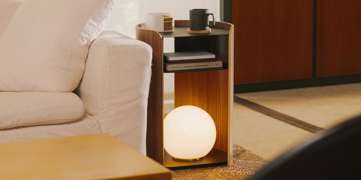 Walnut and black steel modern sidetable holding a globe lamp next to a white couch in a modern living room.